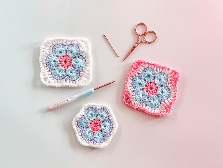 3 African Flower granny squares on an ombre background as a flat lay with scissors a needle and a hook.