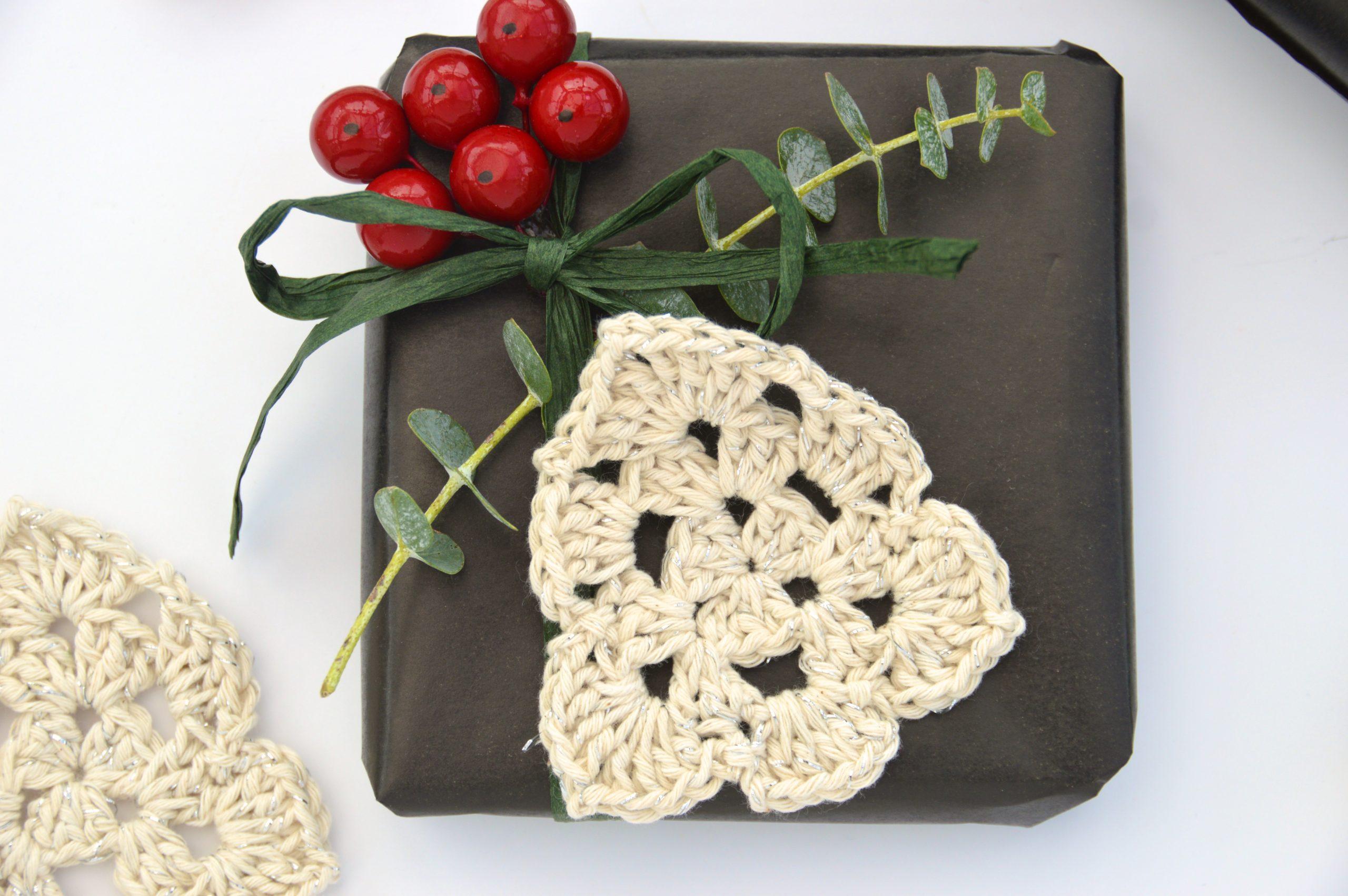 flat lay image of Crochet Christmas Tree made in cream yarn attached to a wrapped present with foliage and berries.