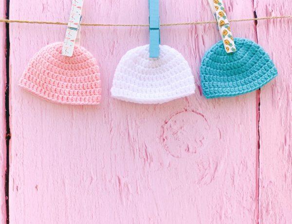 three abby beanie hats pegged up against a pink wooden fence