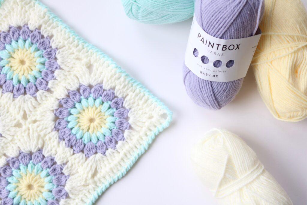 Sunburst granny square as a blanket next to paintbox yarn on a white table.
