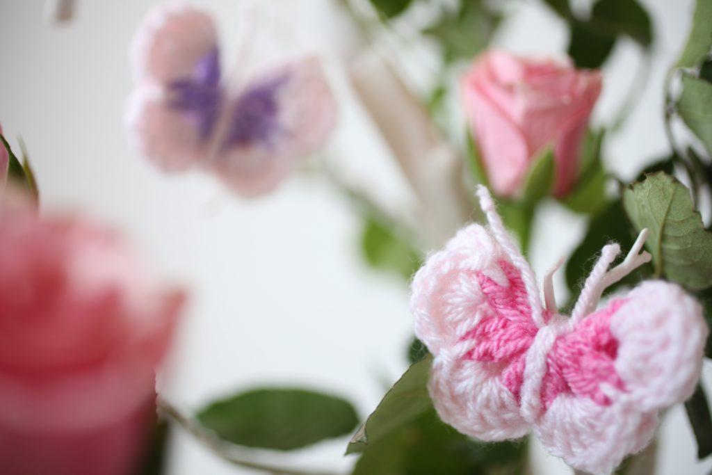 a pair of pastel-coloured crochet butterflies sit in a rose bush