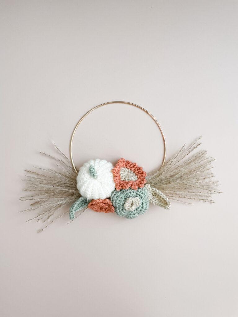 a flat lay image of a crochet pumpkin wreath on a gold hoop with dried flowers splayed out from each side of the cluster crochet pumpkins and flowers.