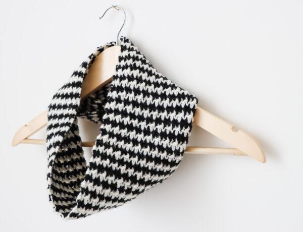 a wooden hanger on a white wall with a black and white houndstooth crochet cowl around the neck of the hanger.