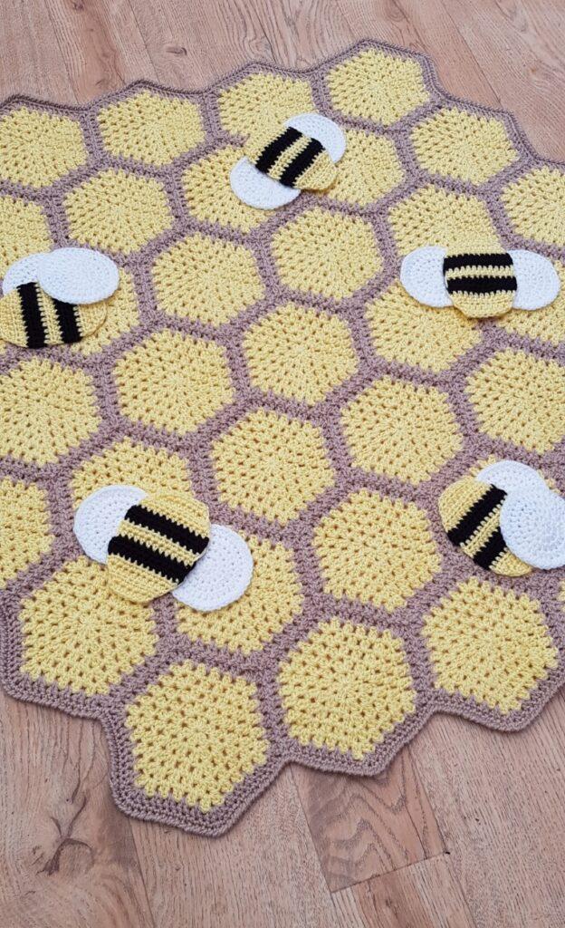 A bee crochet blanket in shades of yellow and brown sits on a wooden floor. 