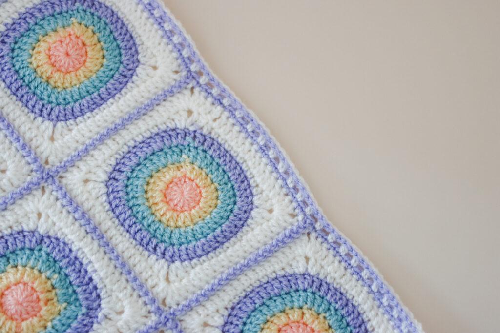 a flat lay image of the circle granny square blanket made in orange, yellow, blue, purple and cream yarn. 