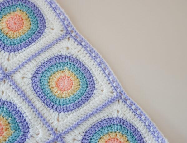 a flat lay image of the circle granny square blanket made in orange, yellow, blue, purple and cream yarn.