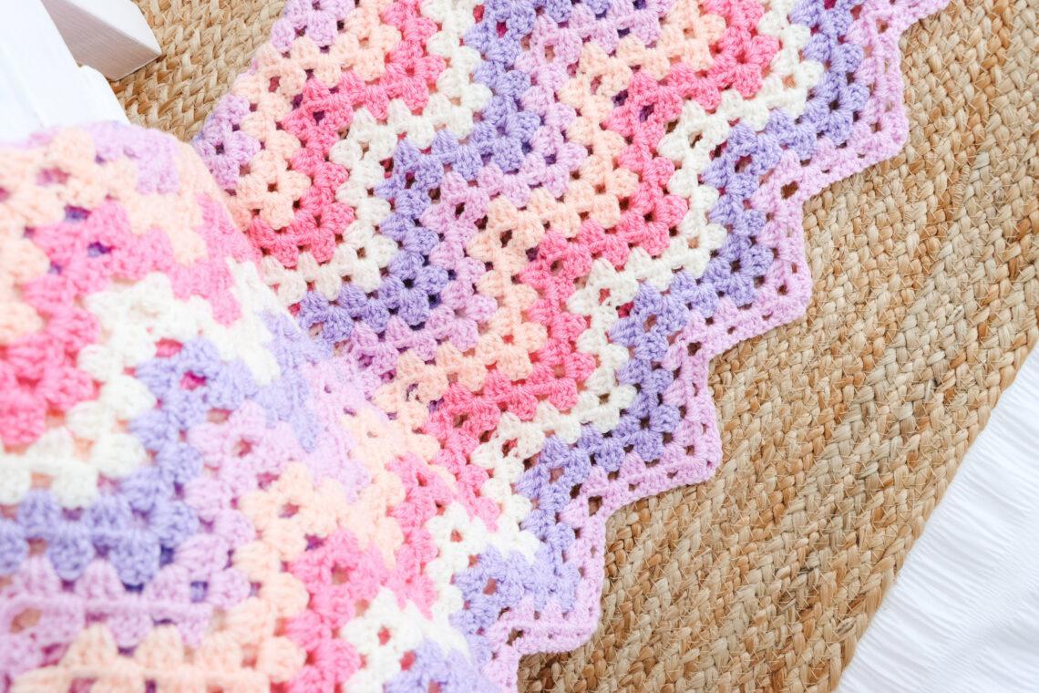 A granny ripple blanket with pink, fuchsia, white, purple and peach stripes.