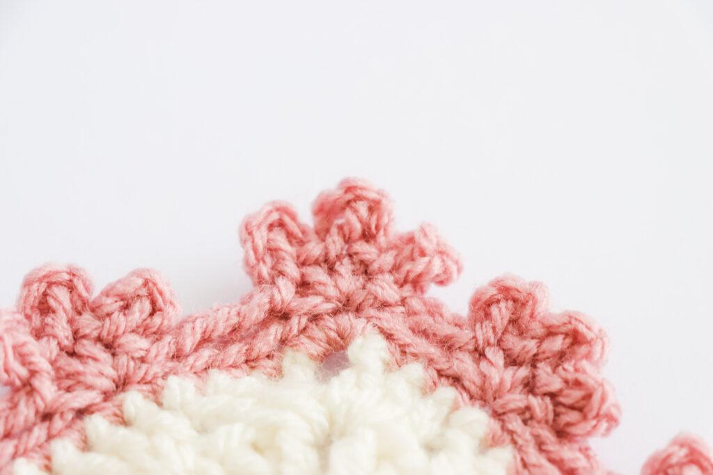A swatch of triple picot edge border is displayed. The swatch is made from white yarn with the border made from a dusty rose colour. 
