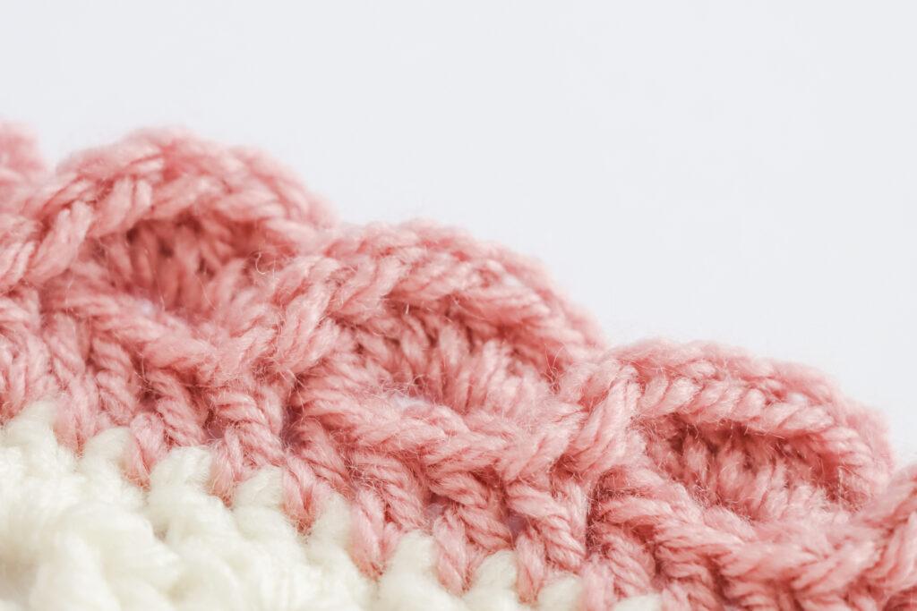 A swatch of wave edge border is displayed. The swatch is made from white yarn with the border made from a dusty rose colour. 