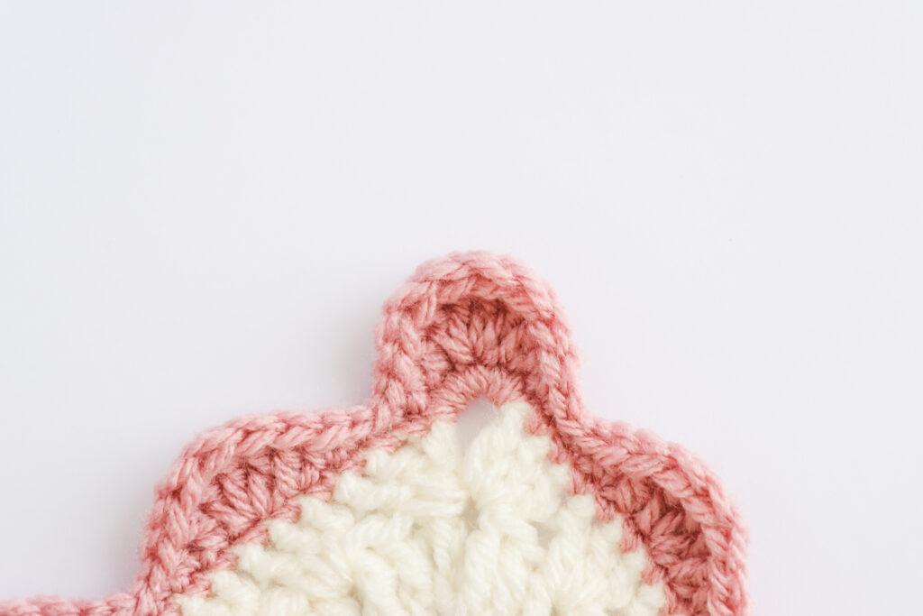 A swatch of  wavy edge border is displayed. The swatch is made from white yarn with the border made from a dusty rose colour. 