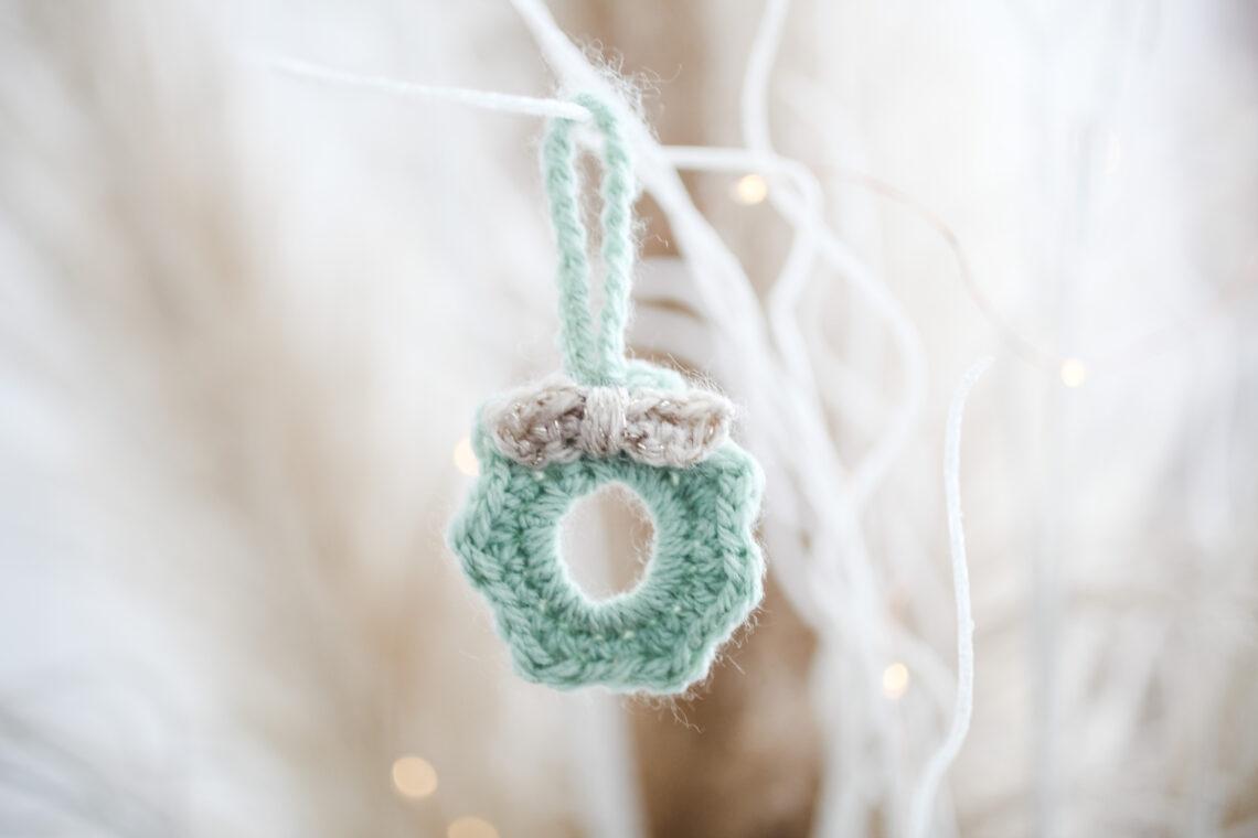 a mini crochet wreath made in pale green yarn with a cream bow hanging from white sparkly branches
