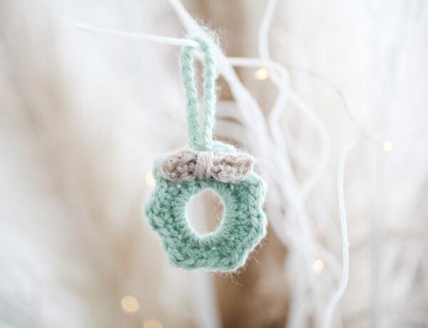 a mini crochet wreath made in pale green yarn with a cream bow hanging from white sparkly branches