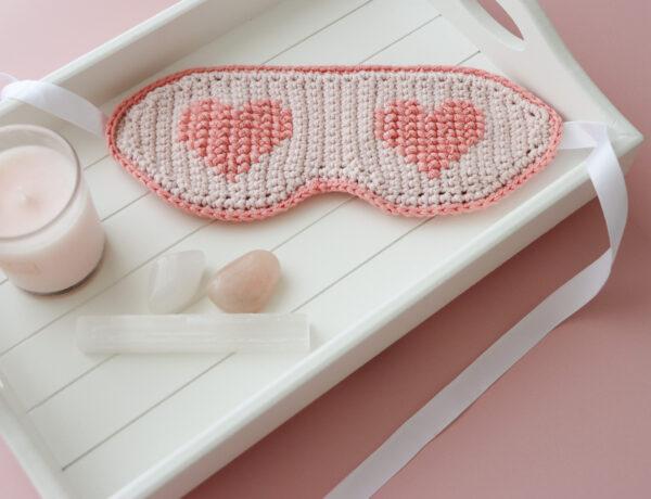 crochet sleep mask ob white tray alongside a pink candle and three crystals