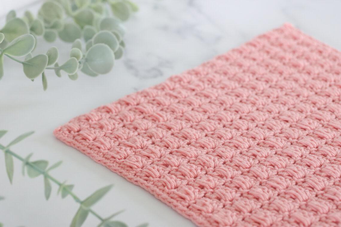 Textured pink crochet swatch made with the blocked bead stitch, displayed on a marble background with eucalyptus decoration.