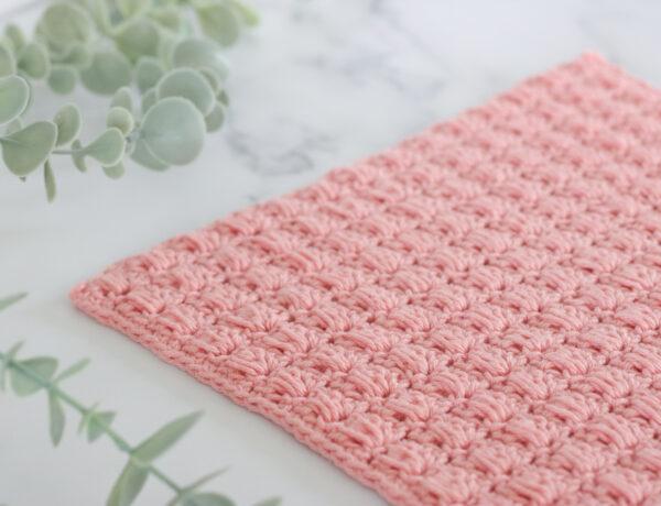 Textured pink crochet swatch made with the blocked bead stitch, displayed on a marble background with eucalyptus decoration.