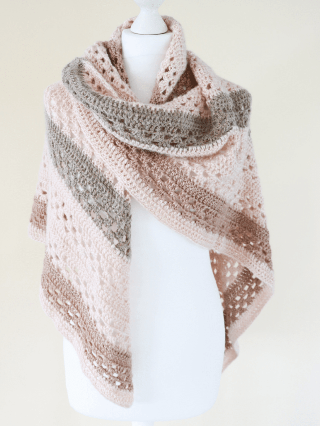 Crochet shawl on a white mannequin in peach, grey and brown yarn.