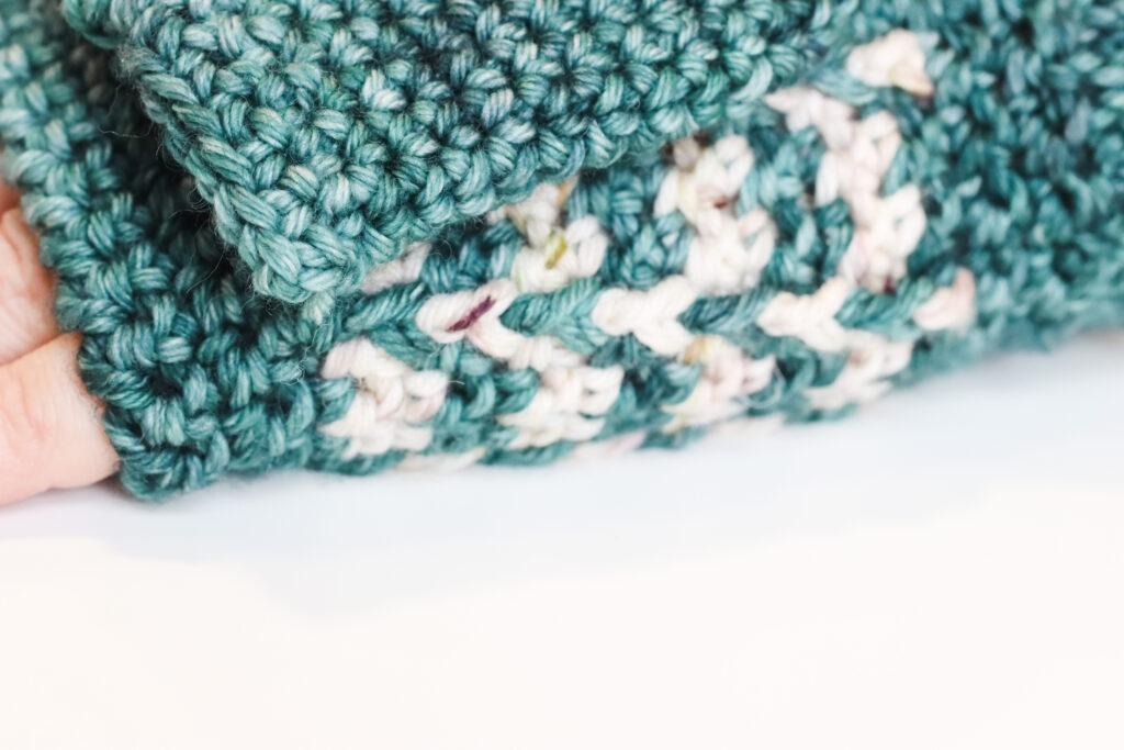 one hand lay flat on a white table wearing a crochet wrist warmer. The image is a close-up on the textured stitch.