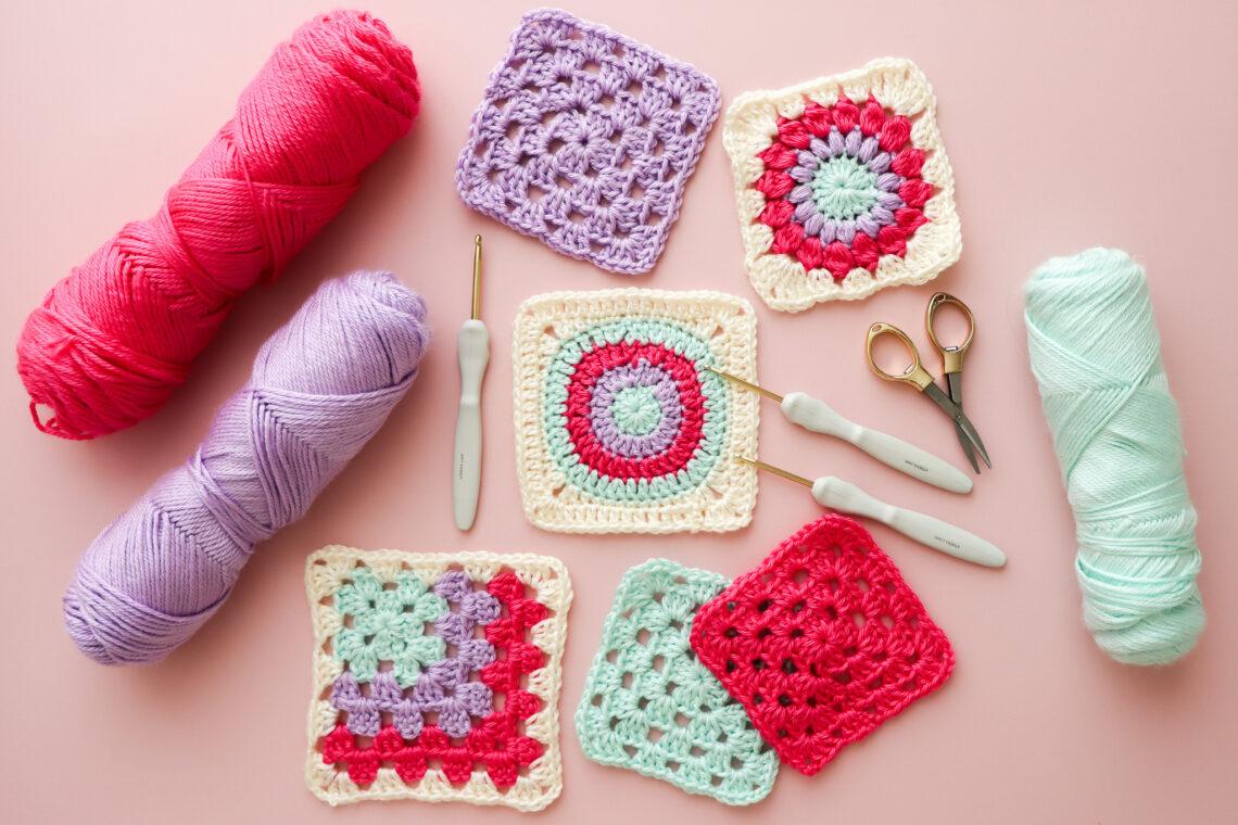 crochet granny squares, yarn and equipment lay flat on a pink background