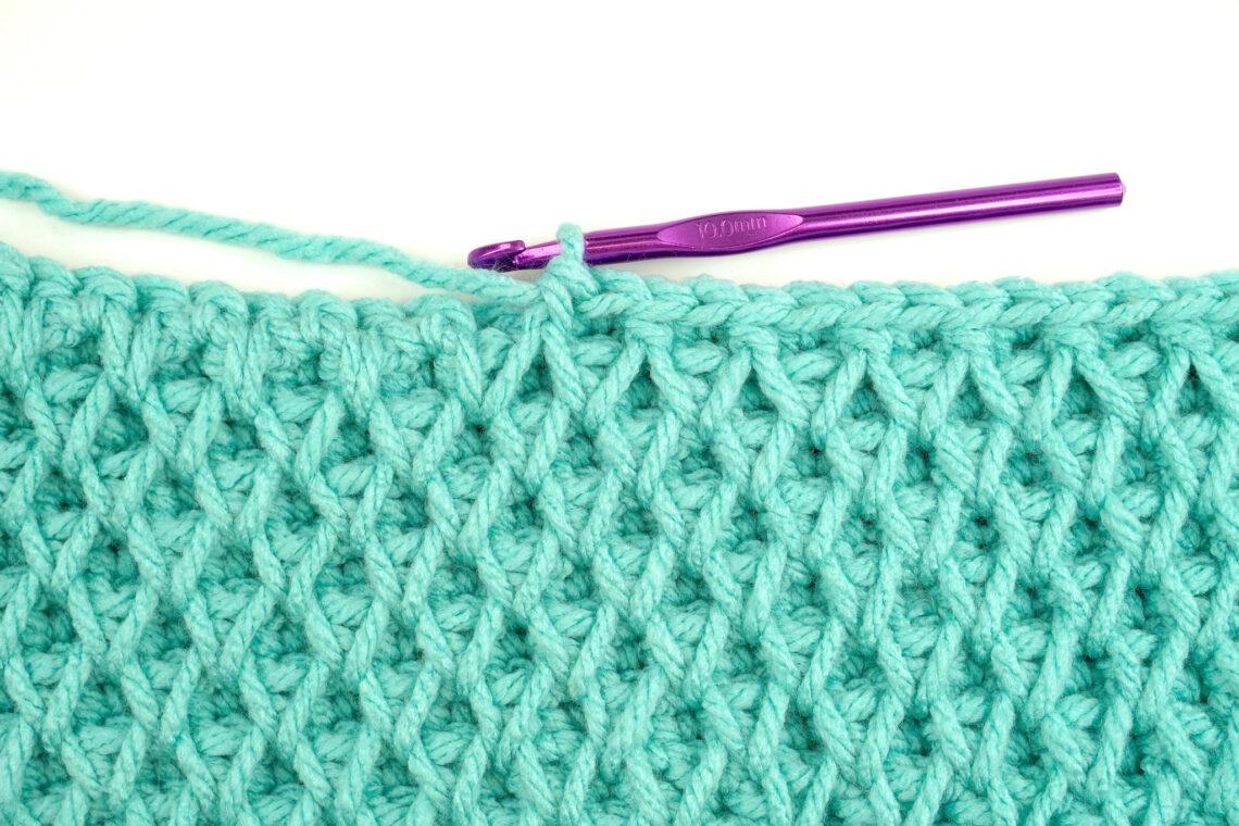 a swatch of honeycomb stitch with aqua yarn and a purple hook