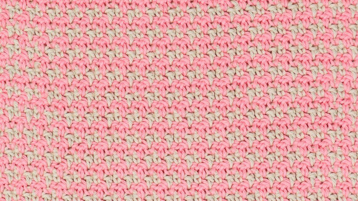 Close-up of a pink and cream crochet swatch demonstrating the houndstooth stitch pattern, showing a repeating, textured design made with alternating colours.