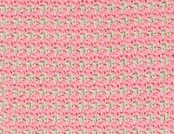 Close-up of a pink and cream crochet swatch demonstrating the houndstooth stitch pattern, showing a repeating, textured design made with alternating colours.