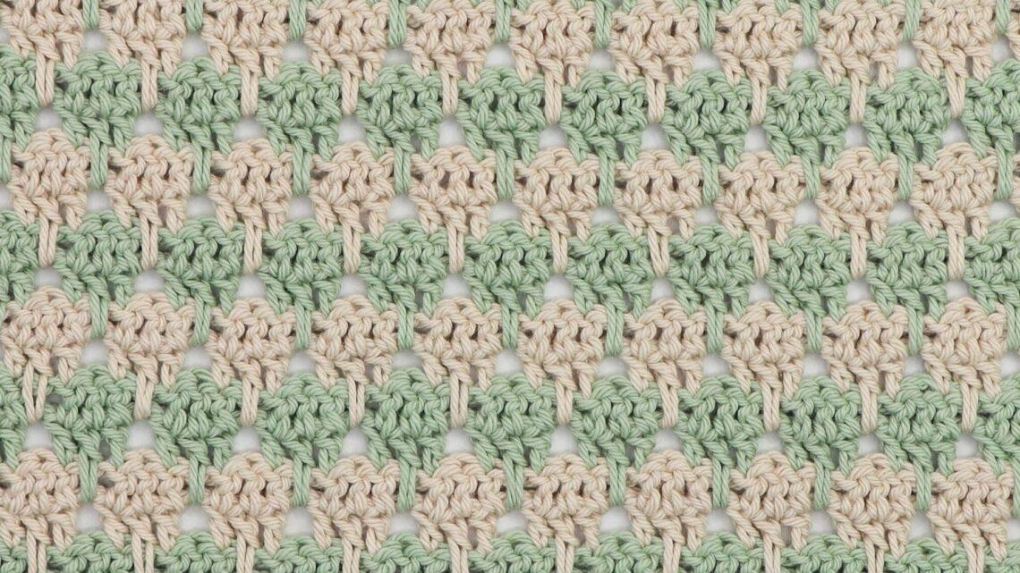 Close-up of crochet larksfoot stitch pattern in alternating rows of sage green and cream yarn. The stitch design features vertical elongated loops resembling bird footprints, creating a textured, repeating geometric pattern.