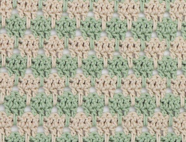 Close-up of crochet larksfoot stitch pattern in alternating rows of sage green and cream yarn. The stitch design features vertical elongated loops resembling bird footprints, creating a textured, repeating geometric pattern.