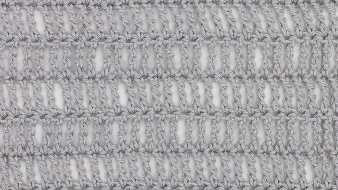 Close-up of a crochet fabric made using the triple treble stitch, showing tall, elongated stitches in light gray yarn with visible vertical gaps for an airy, lacy texture.