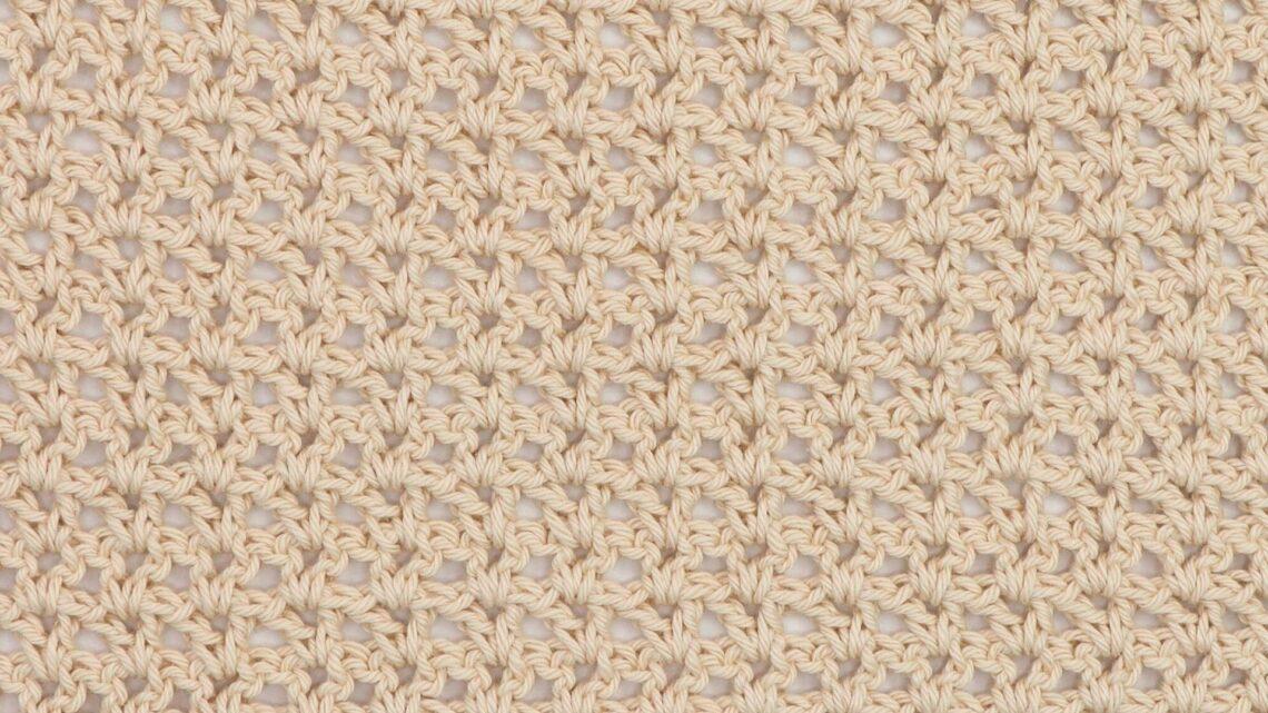 Close-up of a beige crochet swatch using the V-stitch, showing a lacy and open texture with a repeating V-shaped pattern.