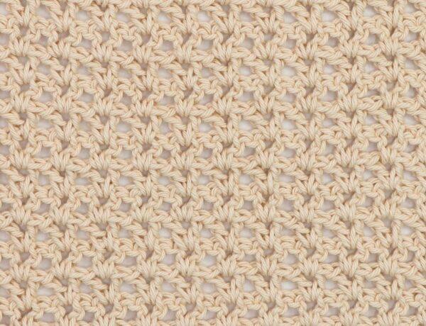Close-up of a beige crochet swatch using the V-stitch, showing a lacy and open texture with a repeating V-shaped pattern.